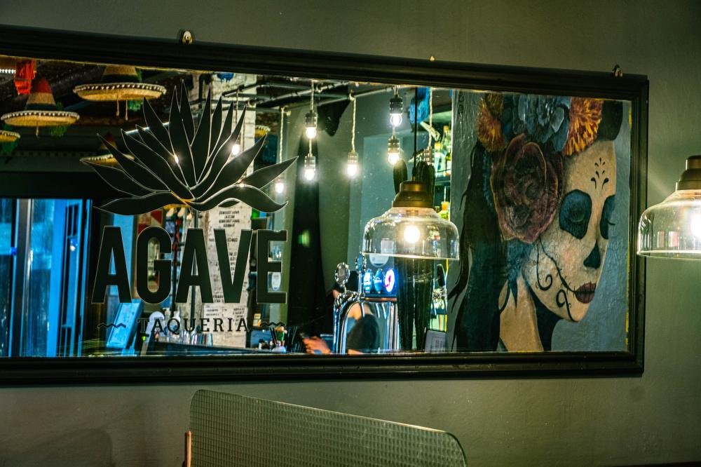 Cartel de neón de AGAVE con el mural de calavera